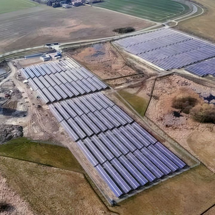 Aerial view of a solar thermal plant with several large collector fields, an operations building and a cylindrical storage tank surrounded by agricultural land.